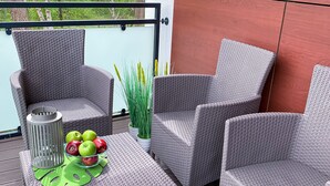 Un balcón con mobiliario de mimbre, una mesa con manzanas y una planta en maceta.