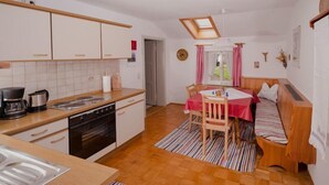 A compact kitchen with a dining area, including a wooden bench and a small table with a red tablecloth. - Ferienwohnung Heuberg mit 1 Separaten Schlafzimmer (Samerberg)