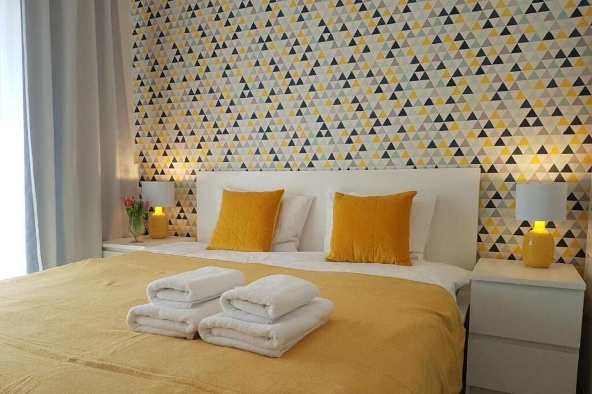 Une chambre d’hôtel avec un lit, deux oreillers, une table de chevet et un mur orné d’un motif géométrique.