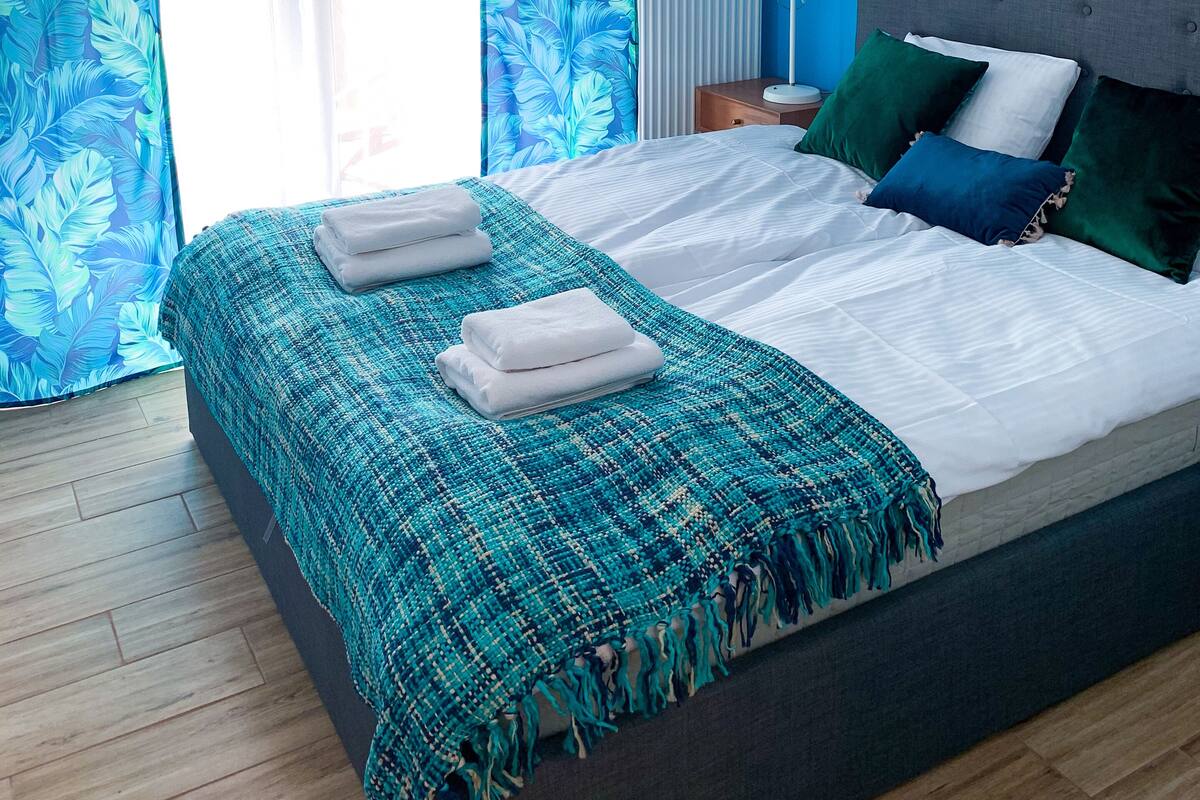 Une chambre à coucher avec un grand lit, une table de chevet, une lampe et une fenêtre avec des rideaux.