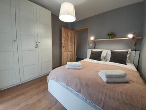 Un dormitorio con cama, armario blanco, puerta de madera y mesita de noche con lámpara.