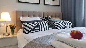 A neatly made bed with striped and solid pillows, a bedside lamp, and a vase of tulips. - Apartamenty Szafirowa Mierzeja - 365PAM (Mielno)