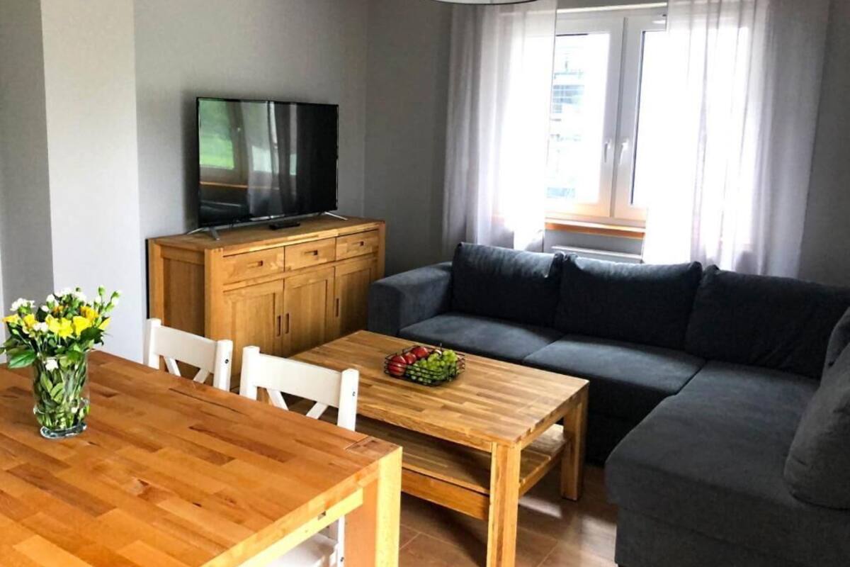Un salon comprenant une table à manger en bois, un canapé, un téléviseur posé sur un meuble en bois et une fenêtre avec des rideaux.