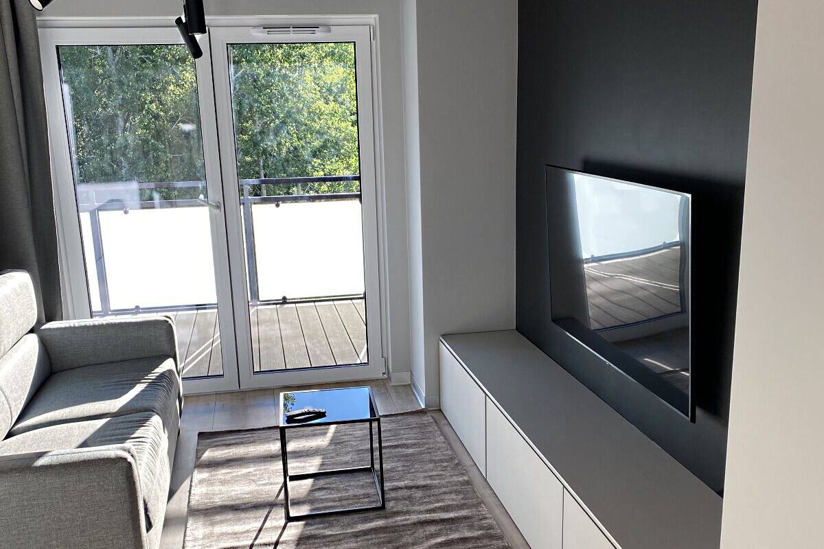 Un salon moderne comprenant un canapé, une table basse, un téléviseur à écran plat fixé au mur et une porte-fenêtre coulissante donnant sur un balcon extérieur.