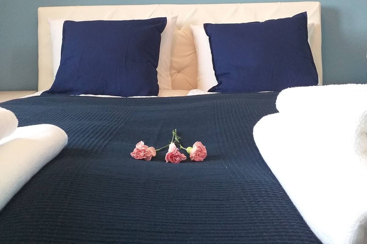 Un lit bien fait, recouvert d’une couvre-lit bleu foncé, avec deux oreillers et une tête de lit blanche.