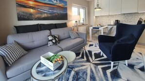A modern living room with a grey sofa, a blue armchair, and a coffee table with a box of tulips. - Apartamenty Szafirowa Mierzeja - 365PAM (Mielno)