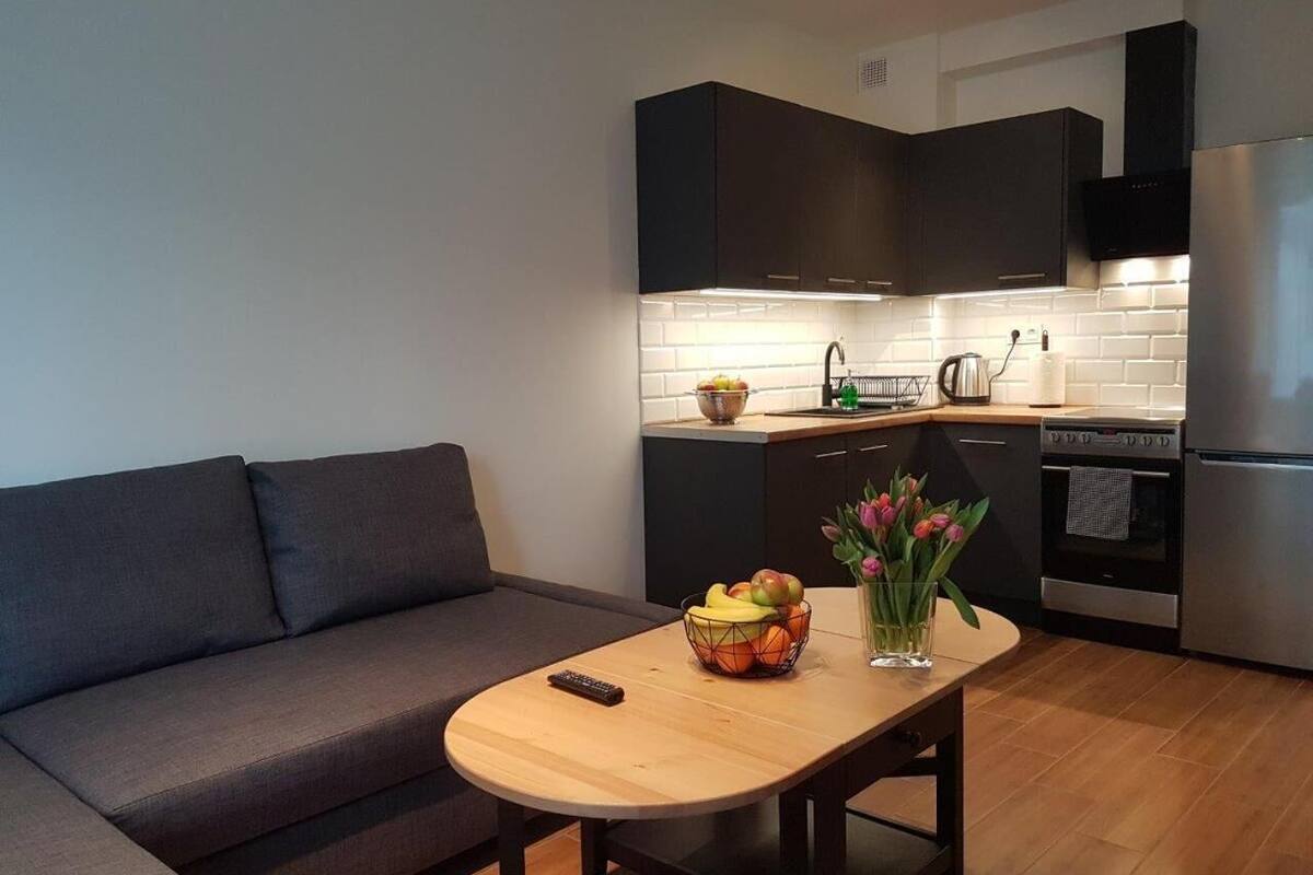 Une cuisine moderne avec des meubles de couleur sombre, une table en bois et un canapé gris.