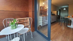 A modern interior with a wooden wall, a glass door leading to a kitchen, and a small dining area with a white table and chairs. - Apartamenty Szafirowa Mierzeja - 365PAM (Mielno)