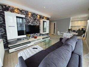 A modern living room with a grey sofa, a flat-screen TV, and a white entertainment unit. - Apartament Różany - 365PAM (Mielno)