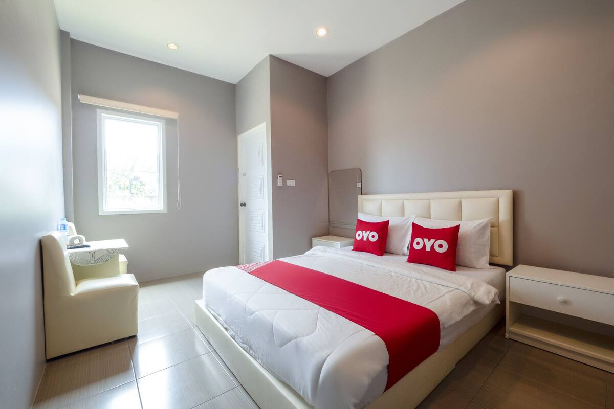 A modern bedroom with a large bed, two bedside tables, a nightstand, a chair, and a window.