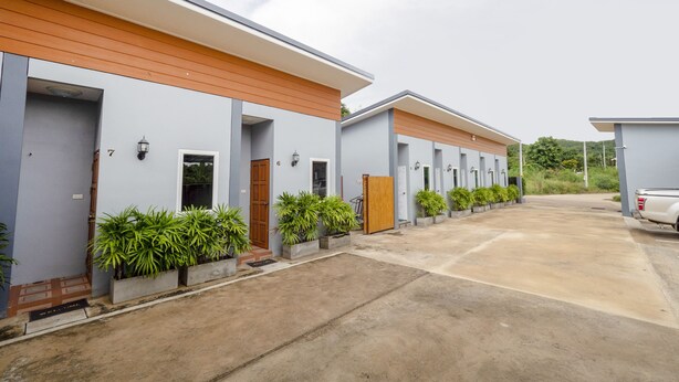 A row of modern, single-story motel buildings with individual entryways, each with a small porch and potted plants. - OYO 1121 Phuree Resort (Sattahip)