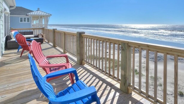Un terrazza in legno con poltroncine Adirondack rosse e blu, una zona relax coperta e vista sull'oceano.