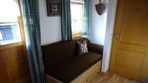 Una habitación acogedora con un banco de madera, un sofá marrón con un cojín estampado con corazones, cortinas a cuadros y una puerta rústica.