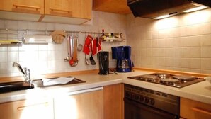 Una cocina con armarios de madera, una estufa, una cafetera y varios utensilios colgados en la pared.