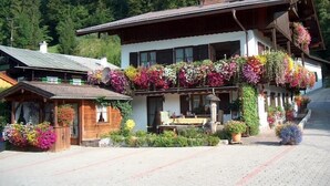 Una cabaña tradicional con un balcón decorado con flores coloridas, fachada de madera y vistas a una ladera boscosa.