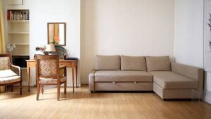Un salon avec un canapé beige, une chaise en bois, une petite table et une bibliothèque.