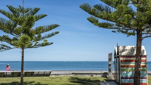 A beach view with a wooden bench, a colorful shed, and a seagull on the grass. - Beautifully renovated studio apartment in Fremantle (Fremantle)