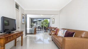 A modern living room with a television, a wooden coffee table, a leather sofa, and a dining area with chairs and a table. - Beautifully renovated studio apartment in Fremantle (Fremantle)