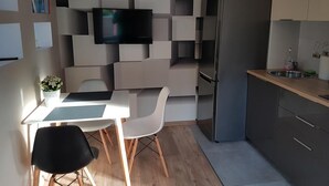 Une cuisine moderne équipée d’un téléviseur encastré, d’un coin repas avec une table et des chaises, et d’un réfrigérateur.