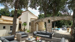 Un'area patio con mobili in vimini, un arco in pietra e una piscina sullo sfondo.