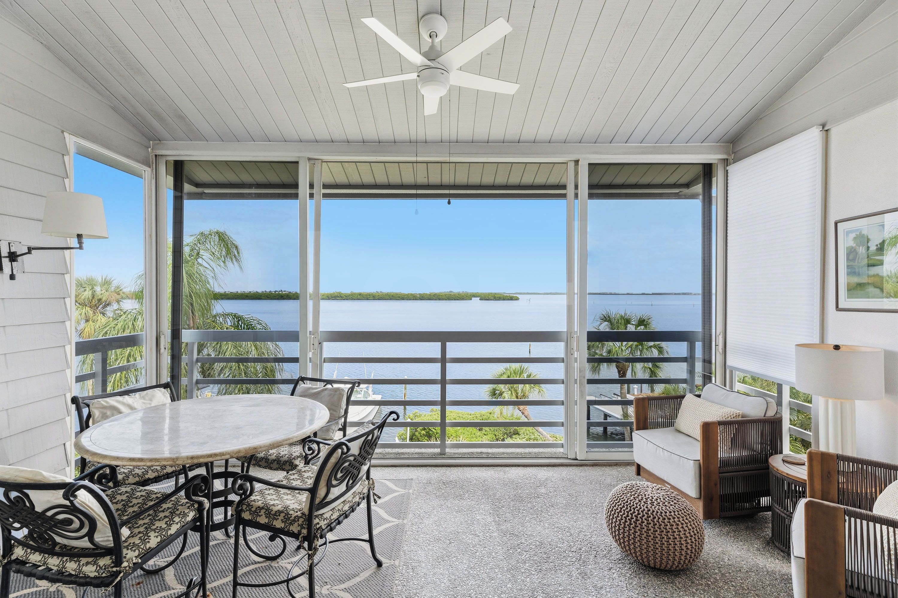A balcony with a table and chairs, a ceiling fan, and a view of a body of water.
