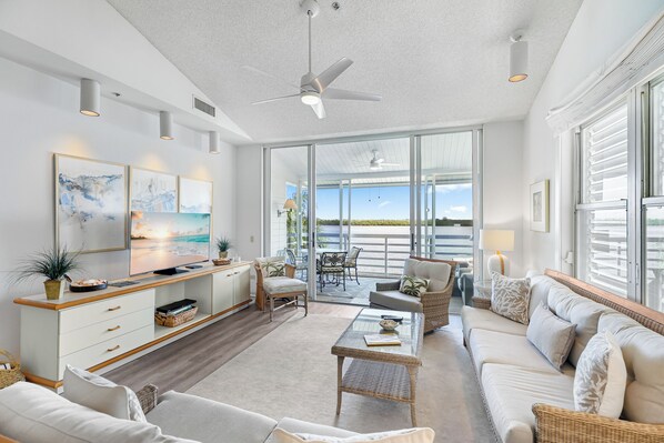 A spacious living area with a large TV, comfortable seating, and a balcony with a view.