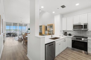 A modern kitchen with white cabinetry, stainless steel appliances, and a view to a dining area with a table and chairs.