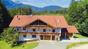 Un chalet de dos plantas con tejado de tejas rojas, balcones de madera con jardineras y un paisaje de montaña de fondo.