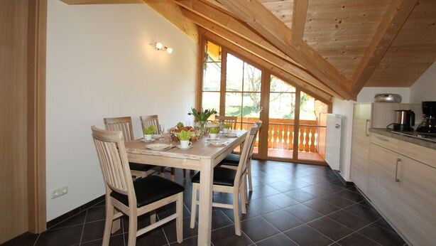 Comedor con una mesa de madera dispuesta para cuatro personas, rodeada de sillas con cojines negros.