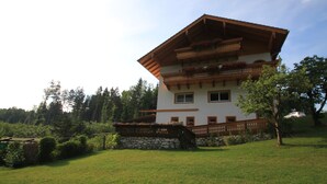 Un edificio de dos pisos con techo inclinado, balcones de madera con jardineras y base de piedra.