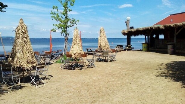 Une plage avec des parasols en chaume, des chaises en bois et un bâtiment doté d’un toit rouge.