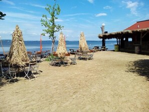 A beach with thatched umbrellas, wooden chairs, and a building with a red roof.