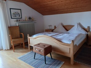 A bedroom with a wooden bed, a chair, a small table, a radiator, and a picture on the wall.