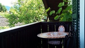 Une petite terrasse extérieure avec une table ronde et deux chaises, entourée d’une balustrade en bois.