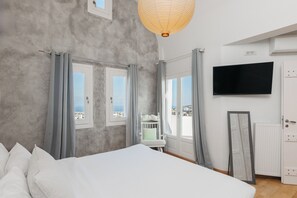 Ein Schlafzimmer mit einem großen Bett, einem Fernseher und Blick auf die Stadt durch die Fenster.