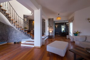 Ein modernes Wohnzimmer mit Treppe, Holzboden, einem weißen Sofa und einem Essbereich.