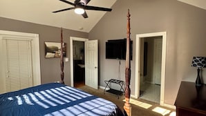 Een slaapkamer met een hemelbed, een plafondventilator, een televisie en een bureau met een lamp.