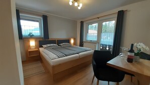 Ett sovrum med en säng i trä, sängbord med lampor, ett litet skrivbord med en stol och ett fönster med gardiner.