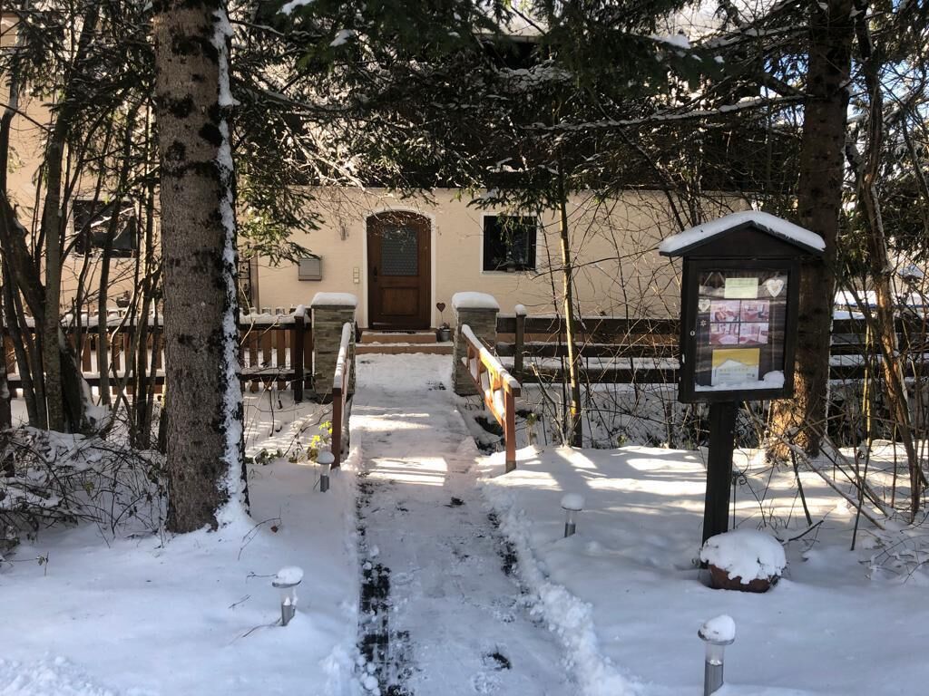 A snow-covered pathway leading to a building with a wooden door and a small structure with a sign.