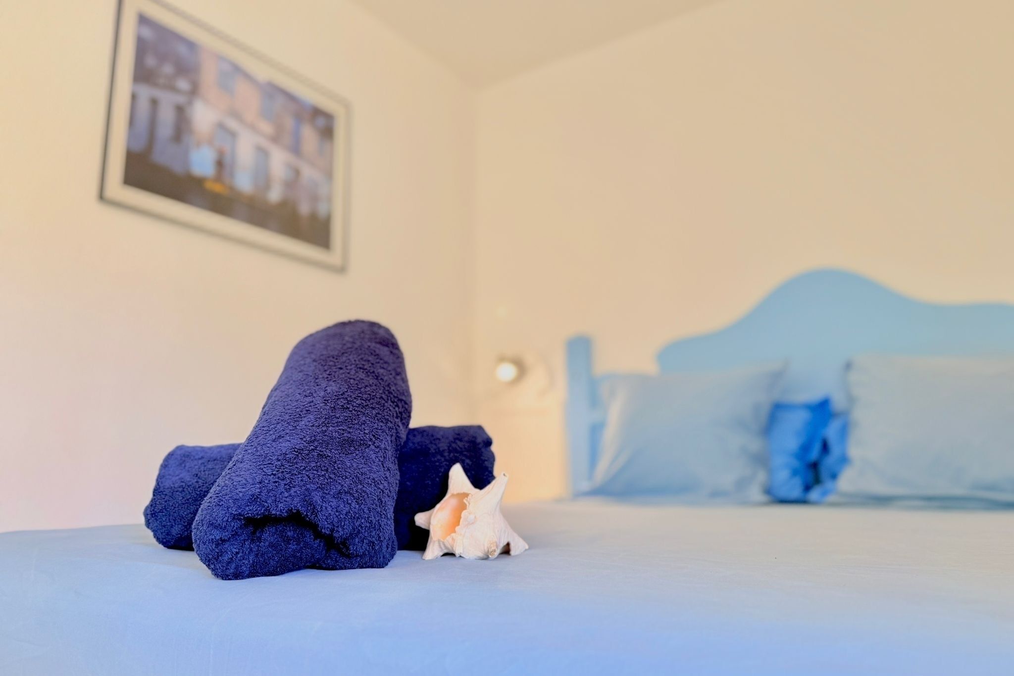 A bed with blue bedding, a small decorative shell, and a framed picture on the wall.