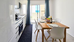 A modern kitchen with a microwave, oven, and sink, a dining area with a table set for two, and a view of the outdoors through a glass door. - Apartment Praia Rocha Vista Mar Summer 1 (Portimão)