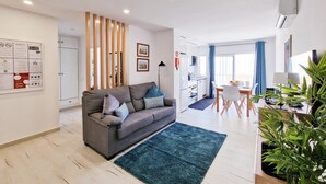 A modern living room with a grey sofa, a blue rug, and a dining area with a table and chairs. - Apartment Praia Rocha Vista Mar Summer 1 (Portimão)