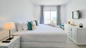 A modern hotel room with a large bed, white furniture, a TV, and a balcony with a view. - Apartment Praia Rocha Vista Mar Summer 1 (Portimão)