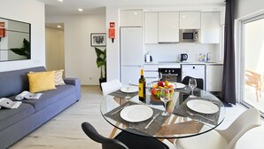 A modern living room with a glass dining table, white chairs, and a sofa with yellow cushions. - Apartment Praia Rocha Vista Mar Summer 2 (Portimão)