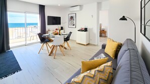 A modern living room with a dining area, a sofa with patterned cushions, and a view of the sea through large windows. - Apartment Praia Rocha Vista Mar Summer 2 (Portimão)