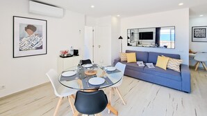 A modern living room with a glass dining table, a blue sofa, and a mounted TV. - Apartment Praia Rocha Vista Mar Summer 2 (Portimão)