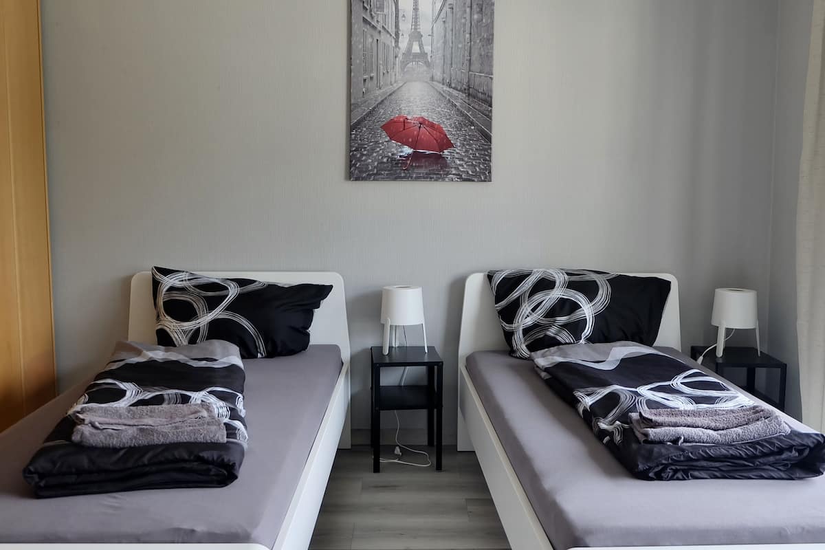 A hotel room with two beds, each with a pillow and a bedside table with a lamp.