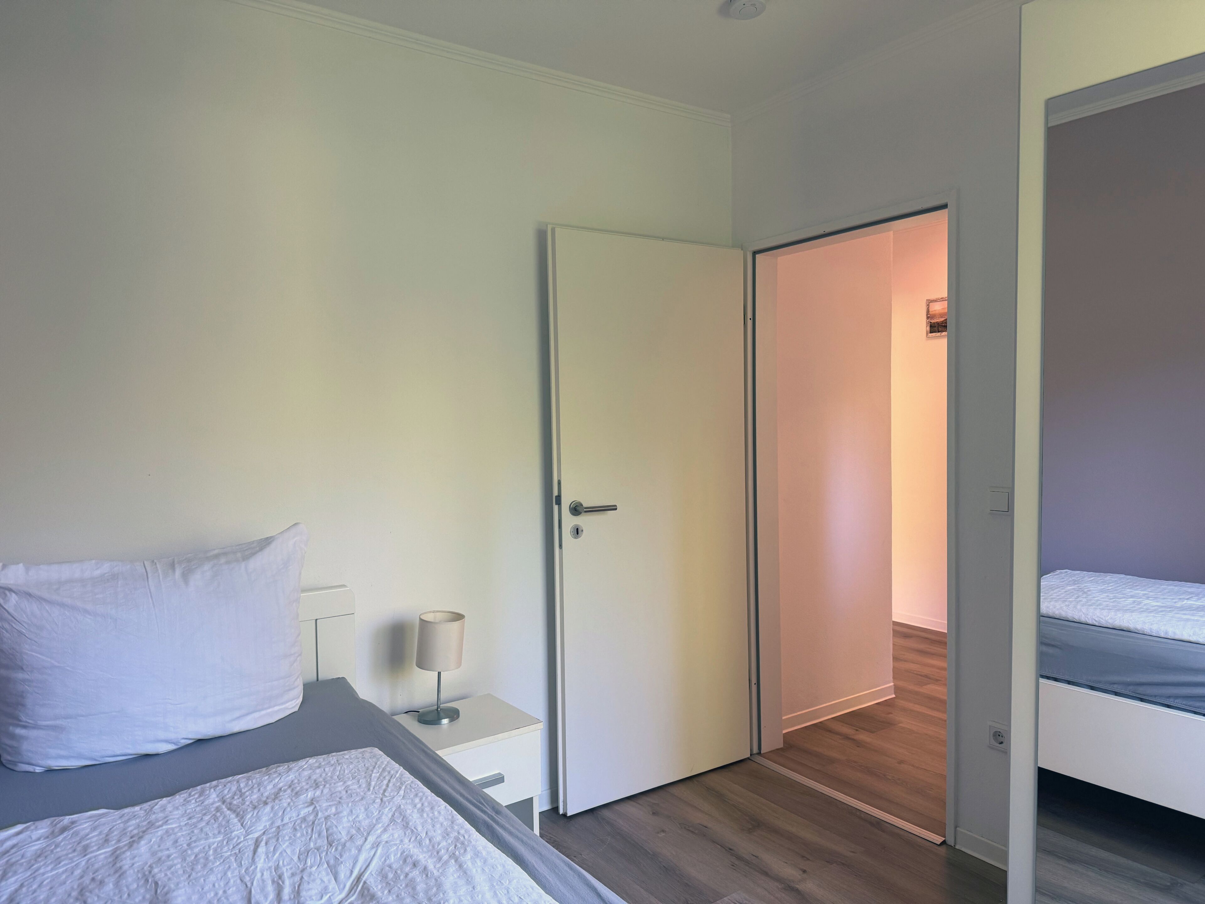 Une chambre à coucher comprenant un lit, une table de chevet, une lampe et une porte donnant sur une autre pièce.