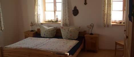 Ein Schlafzimmer mit einem hölzernen Bett, zwei Nachttischen, einem Fenster mit Vorhängen und einem an der Wand befestigten Kruzifix.
