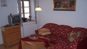 Ett vardagsrum med en byrå i trä, en tv ovanpå den, en röd soffa med mönster, ett litet träbord och en tavla på väggen.